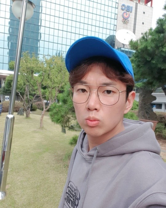 Jang Sung-gyu se está tomando una selfie mientras usa una sudadera con capucha